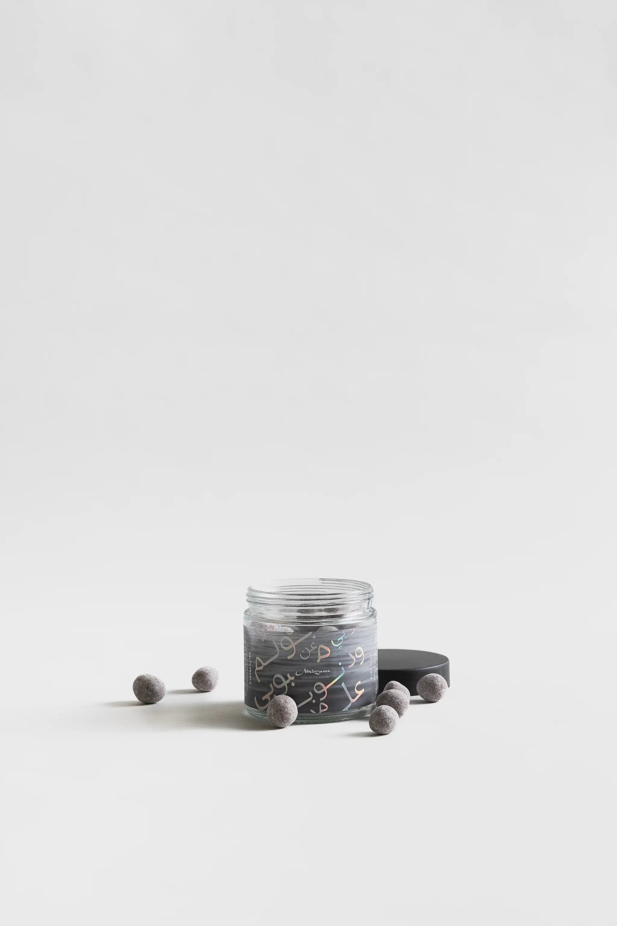 A jar of grey spherical candies with black lid and Arabic script design.